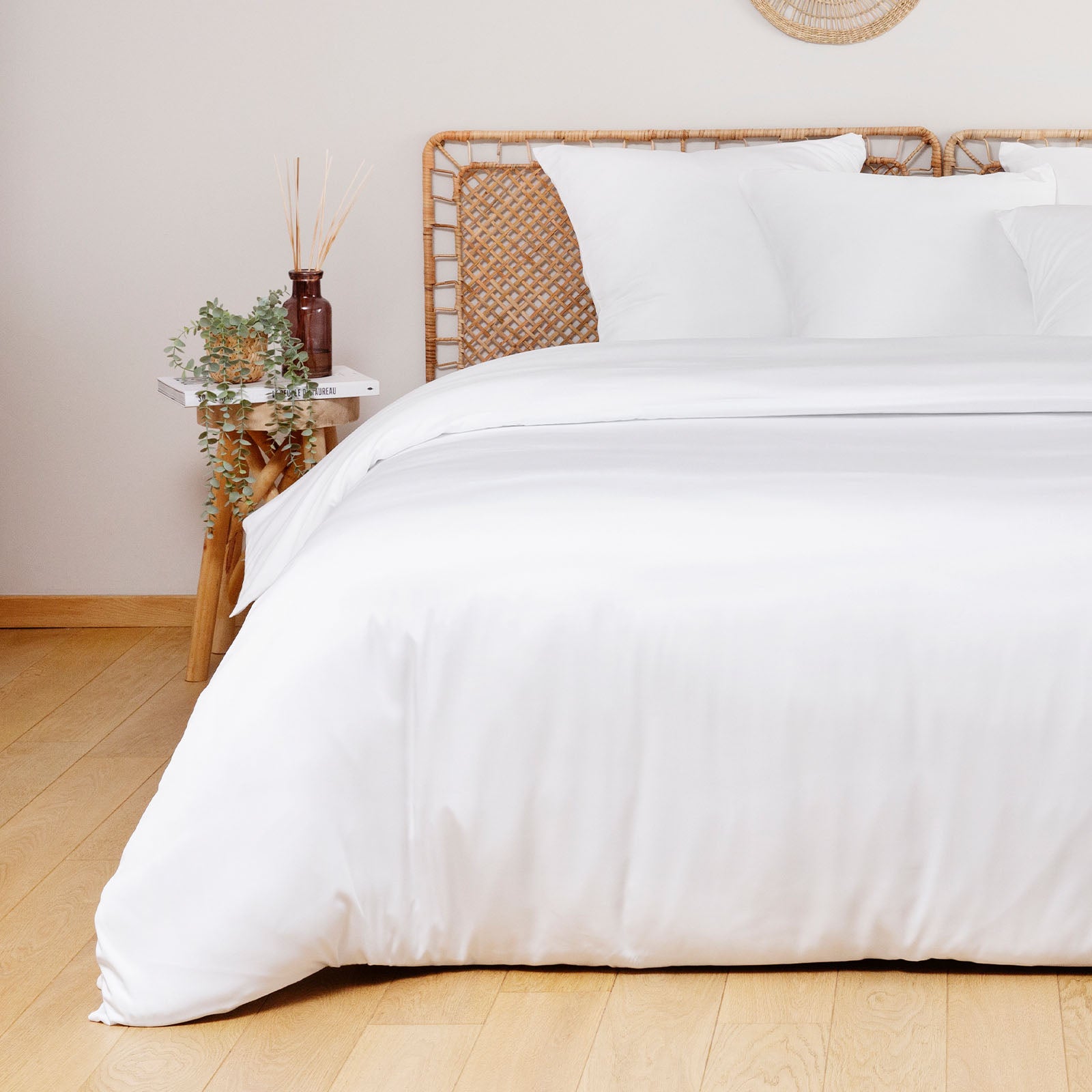 White comforter on a bed with a wooden headboard and side table in a room.