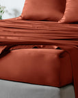 bambaw cozy terracotta fitted sheets and pillows on a bed with a neutral background