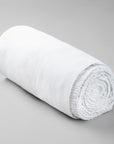 Rolled-up white bamboo fitted sheet on a gray background