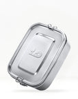 Stainless steel lunch box with its clasp and a tall metal bottle visible behind on a light background