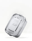 Close up of a stainless steel lunch box lid with a metal clasp against a light background