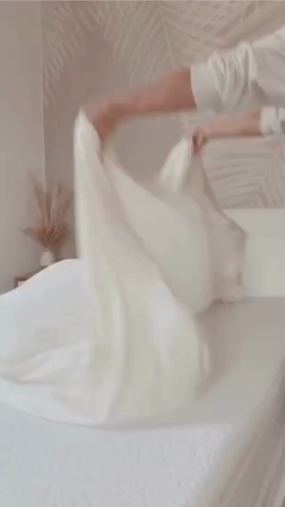 a video of a woman making a bed with white bamboo fitted sheet