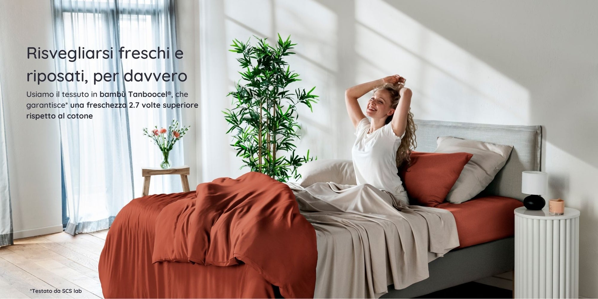 Donna che si sveglia in una camera da letto luminosa con biancheria da letto in bambù terracotta di Bambaw e pareti bianche.